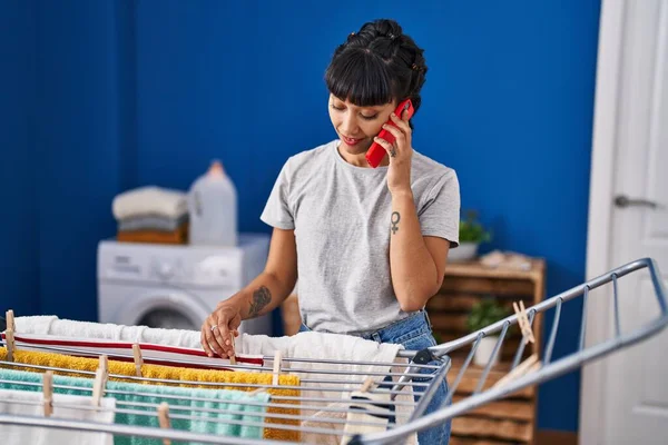Mujer Joven Hablando Teléfono Inteligente Colgando Ropa Lavandería —  Fotos de Stock