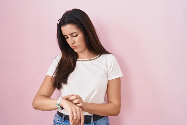 若いですブルネット女性立っています上のピンクの背景チェックザ時間上の手首腕時計 リラックスして自信 — ストック写真