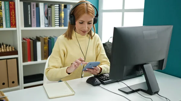 大学の教室で勉強しているスマートフォンやヘッドフォンを使用して若いブロンドの女性の学生 — ストック写真