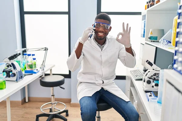 アフリカ系アメリカ人の男性科学者研究所で働いている指でOkサインをする電話で話す 笑顔優しいジェスチャー優れたシンボル — ストック写真