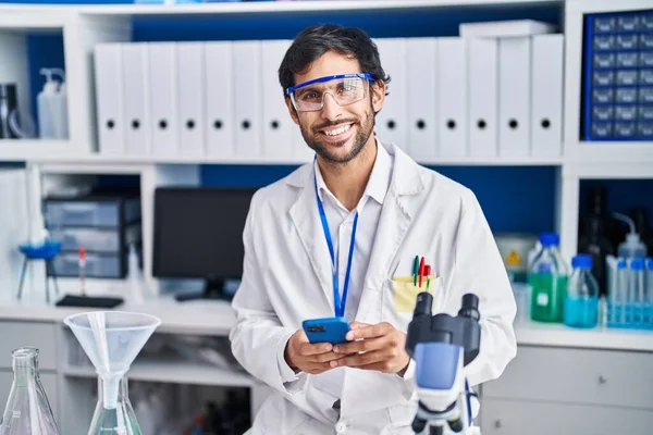 Young Hispanic Man Scientist Smiling Confident Using Smartphone Laboratory — Stock fotografie