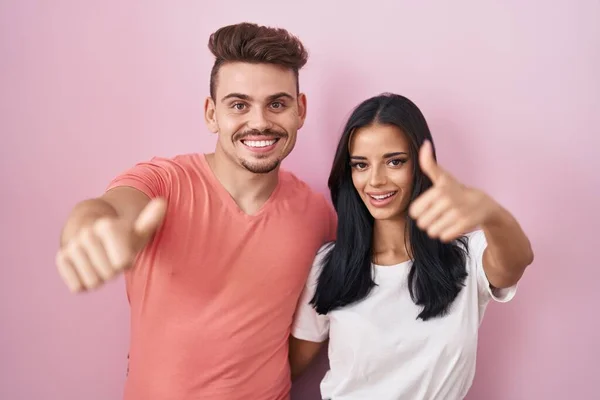 Young Hispanic Couple Standing Pink Background Approving Doing Positive Gesture — Stock Photo, Image