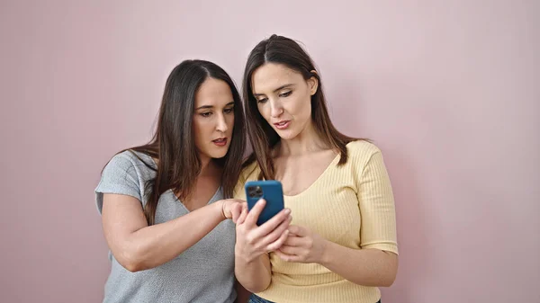 Δύο Γυναίκες Που Χρησιμοποιούν Smartphone Σοβαρή Έκφραση Απομονωμένο Ροζ Φόντο — Φωτογραφία Αρχείου
