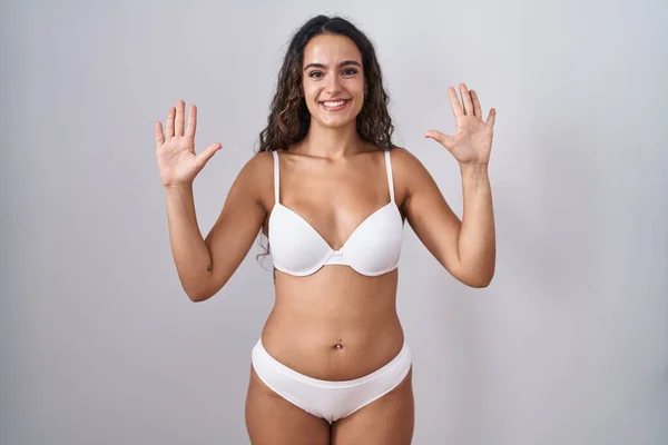 Young hispanic woman wearing white lingerie showing and pointing up with fingers number ten while smiling confident and happy.