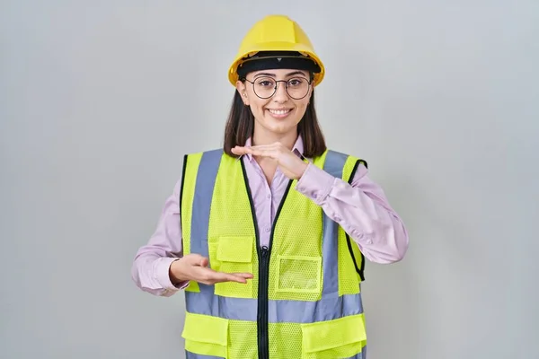 西班牙裔女孩身穿建筑工人制服 手拿着安全帽 手举着大号和大号的标志 测量符号 微笑着看着摄像机 计量概念 — 图库照片