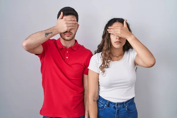 Young Hispanic Couple Standing Isolated Background Covering Eyes Hand Looking — Stock Photo, Image