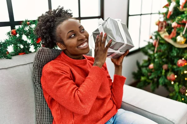 African American Woman Holding Christmas Gift Sitting Sofa Home — Zdjęcie stockowe