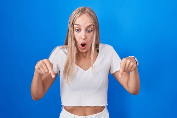 Mladá Běloška Stojí Nad Modrým Pozadím Ukazuje Prstem Reklamu Překvapenou — Stock fotografie