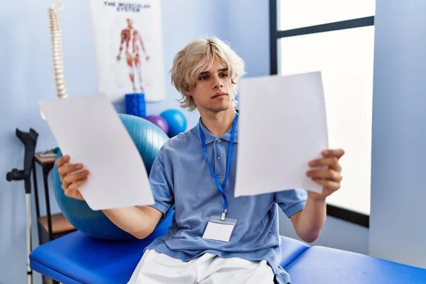 Jovem Loiro Pisioterapeuta Leitura Documento Sentado Quadro Massagem Clínica Reabilitação — Fotografia de Stock