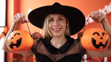 Young blonde woman having halloween party holding pumpkin baskets at home