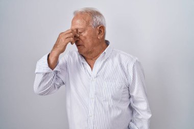 İzole edilmiş arka planda gri saçlı yaşlı adam yorgun burnu ve gözleri ovuşturup yorgun ve baş ağrısı çekiyor. Stres ve hüsran kavramı. 