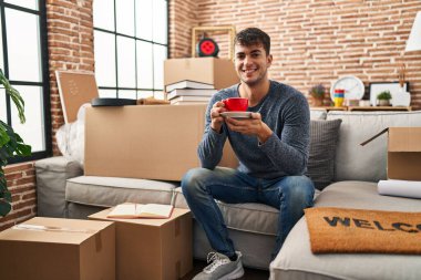 Genç İspanyol adam yeni evindeki kanepede kahve içiyor.