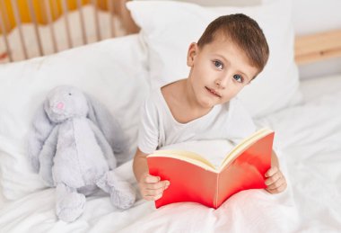 Sevimli beyaz çocuk kitap okuyor yatak odasında oturuyor.
