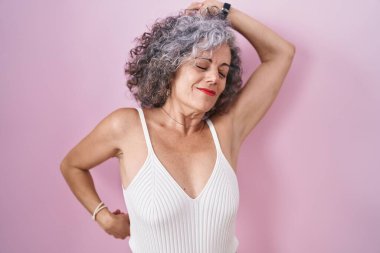 Middle age woman with grey hair standing over pink background stretching back, tired and relaxed, sleepy and yawning for early morning 
