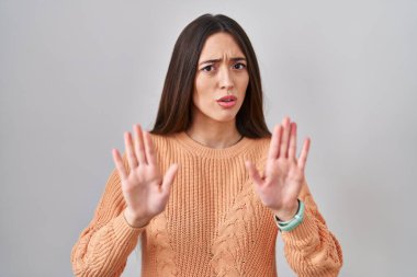 Beyaz arka planda duran esmer bir kadın. Avuçlarını hareket ettiriyor. Korkmuş ve iğrenç bir ifadeyle reddediyor. Dur ve yasakla. 