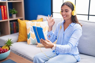 Genç İspanyol kadın, tabletle video görüşmesi yapıyor, kulaklık takıyor, parmaklarıyla imza atıyor, gülümseyerek mükemmel bir sembol oluşturuyor. 