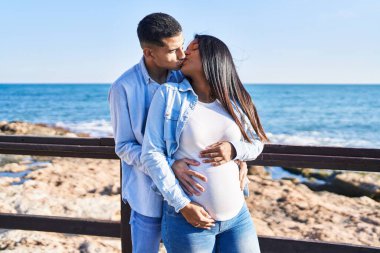 Genç, Latin bir çift bebek bekliyor. Birbirlerine sarılıyorlar ve deniz kenarında öpüşüyorlar.