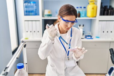 Laboratuvarda pipet kullanan, bilim adamı üniforması giyen İspanyol genç bir kadın.