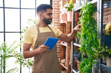 Young arab man florist smiling confident using touchpad at florist