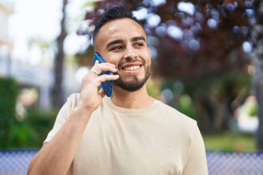 Genç İspanyol adam gülümsüyor. Parktaki akıllı telefondan konuşuyor.