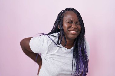 Genç Afrikalı kadın pembe arka planda duruyor sırt ağrısı çekiyor, elleriyle dokunuyor, kas ağrısı çekiyor. 
