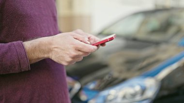 Genç İspanyol adam akıllı telefon kullanıyor. Arabasının yanında bekliyor.