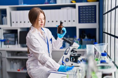 Young caucasian woman scientist write on document holding bottle at laboratory