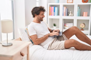 Yatak odasında dizüstü bilgisayar kullanan genç bir İspanyol.