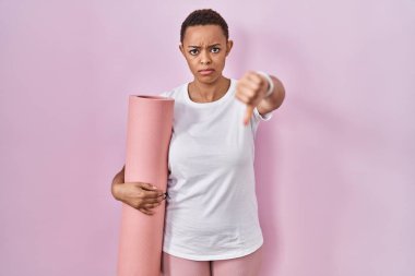 Güzel Afrikalı Amerikalı kadın yoga minderini tutarken mutsuz ve kızgın görünüyor. Reddedilmiş ve olumsuz bir hareket yapıyor. kötü ifade. 