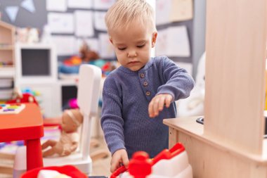 Anaokulunda rahat bir ifadeyle oynayan sevimli beyaz çocuk.