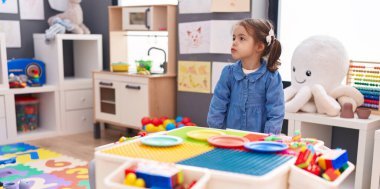 Adorable hispanic girl standing with relaxed expression at kindergarten