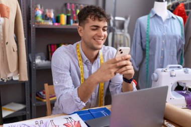 Genç İspanyol terzi atölyede akıllı telefon ve dizüstü bilgisayar kullanıyor.