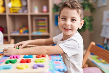Anaokulunda masada oturmuş matematik oyunu oynayan sevimli beyaz çocuk.