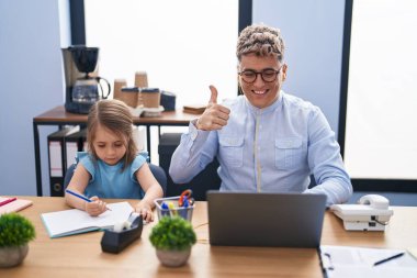 Ofiste birlikte çalışan genç bir baba ve kız mutlu ve pozitif gülümsüyor, başparmağıyla mükemmel ve onay işareti yapıyor. 