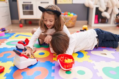 Süpermarket oyunu oynayan sevimli bir çocuk ve kız anaokulunun zemininde oturuyorlar.