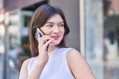 Beyaz bir kadın gülümsüyor ve caddede akıllı telefondan konuşuyor.