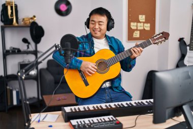 Young chinese man guitarist playing classical guitar at music studio