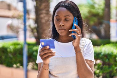 Genç Afro-Amerikalı kadın akıllı telefondan konuşuyor ve park yerinde kredi kartı kullanıyor.