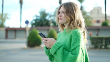 Sokakta akıllı telefon kullanan, kendine güvenen genç sarışın kadın.