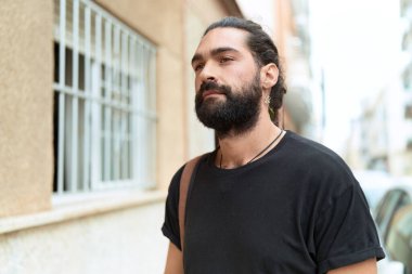 Latin kökenli genç adam ciddi bir ifadeyle sokağa bakıyor.