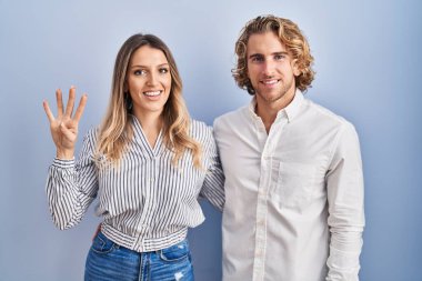 Mavi arka planda duran genç çift, mutlu ve kendinden emin gülümserken dört numarayı gösteriyor ve işaret ediyor.. 