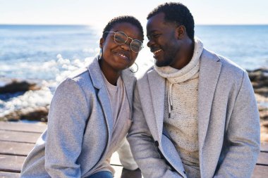 Kadın ve erkek, sırıtıyor. Sahilde oturuyorlar.