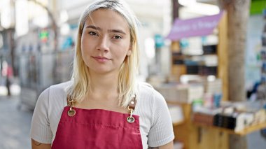 Genç, güzel, İspanyol bir kadın gazete bayiinde rahat bir ifadeyle önlük giyiyor.