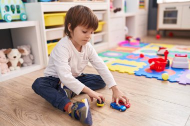 Beyaz tenli sevimli bir çocuk anaokulunda yerde oturmuş oyuncaklarla oynuyor.