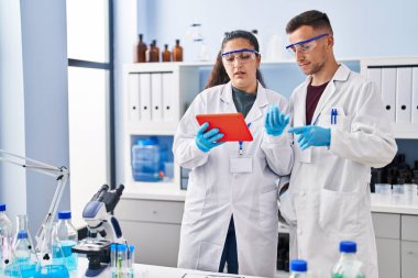 Man and woman wearing scientist uniform using touchpad at laboratory