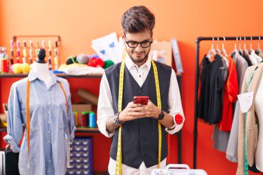 Genç İspanyol terzi atölyedeki akıllı telefonu kullanarak gülümsüyor.