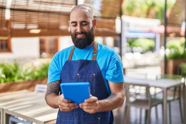 Young bald man waiter smiling confident using touchpad at coffee shop terrace