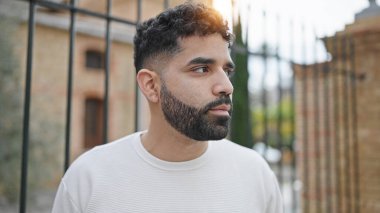 Latin kökenli genç adam ciddi bir ifadeyle sokağa bakıyor.