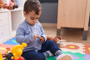 Sevimli İspanyol çocuk anaokulunda yerde oturan aletlerle oynuyor.