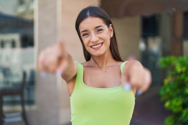 Genç ve güzel İspanyol kadın gülümsüyor. Kendine güveni tam. Sokakta kamerayı işaret ediyor.